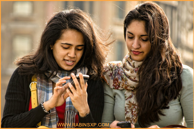 Two Girls testing the features of a mobile phone before buying.